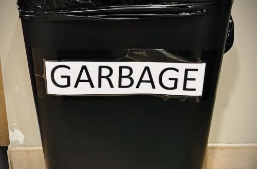 A black three gallon trash can with black liner bag labeled "Garbage," typed in all caps on white paper.